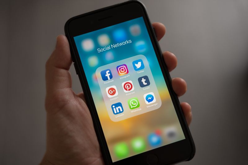 A smartphone displaying various social media icons held in a hand